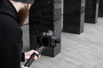 Bearded Professional videographer in black hoodie holding professional camera on 3-axis gimbal...