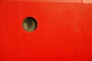 Round porthole in the hull. The steel hull of the ship is painted red.