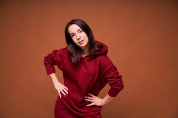 Young happy and positive woman in red hoodie standing on brown background