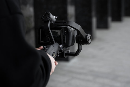 Professional videographer in black hoodie holding professional camera on 3-axis gimbal stabilizer. Filmmaker making a great video with a professional cinema camera. Cinematographer.