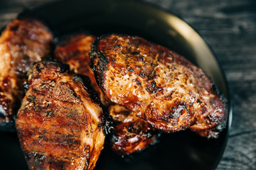 A black plate full of smoked pork chops from an outdoor barbecue grill smoker