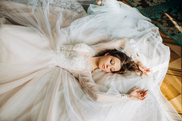 Cute bride in a pastel dress lies on the bed with her eyes closed