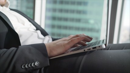 Successful businessman in the office against the background of a pan-window with skyscrapers. A businessman is lying in a comfortable chair with a beech laptop on his lap.