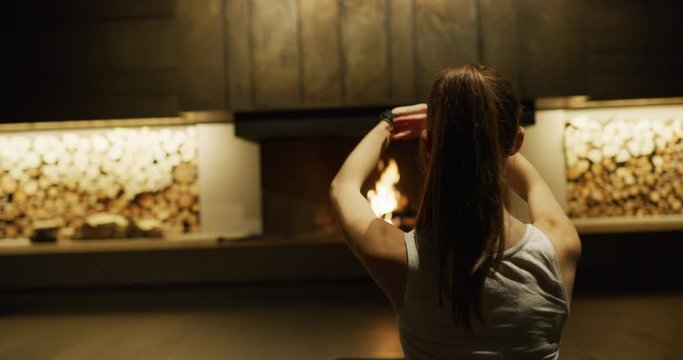 Close up of an young rich woman is doing yoga and relaxing her mind in a luxury cosy apartment with a fireplace in the evening. Shot in 8K. Concept: relax,comfort, warm ambient, luxury interior design