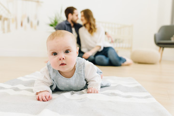 Caucasian baby crawling on the floor of nursery with her parents in the background