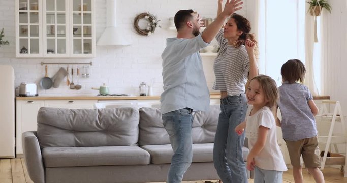 Carefree family young parents and cute little children dancing to music having fun together in modern kitchen interior, funny happy mother father with kids enjoying leisure lifestyle activity at home