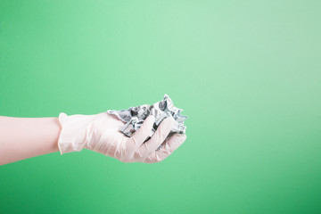 hand in a rubber white medical disposable glove holds crumpled dollar bills on a green background copy space