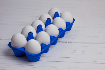 ten white eggs in blue uniform on a wooden light background