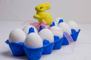ten white eggs in a blue uniform and a yellow Easter rabbit with a pink bow on a wooden light background