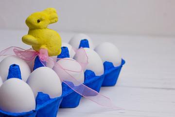ten white eggs in a blue uniform and a yellow Easter rabbit with a pink bow on a wooden light background