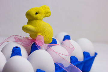 ten white eggs in a blue uniform and a yellow Easter rabbit with a pink bow on a wooden light background