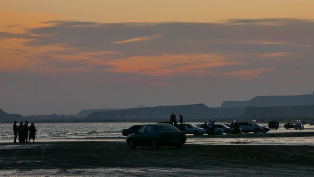 Long shot of row of silhouette cars can people standing near the sea in beach at sunset