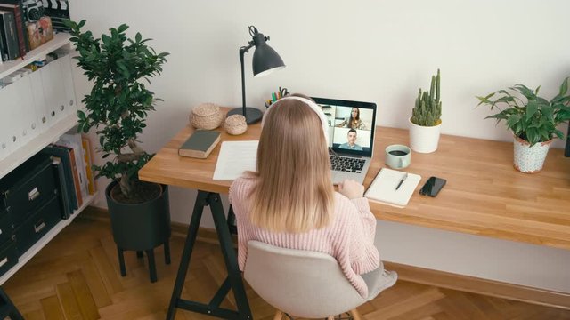 Online Group Video Call Conference of Work Team from Home Office. Woman in Headphones Greets and Talks with 4 People at Video Chat using Laptop. Self-isolation at Pandemic. 4K Top View Wide Orbit Shot