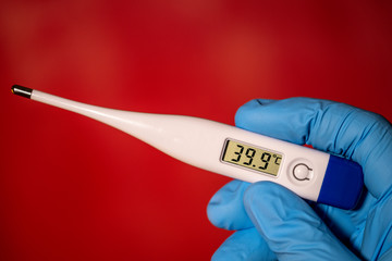 Obraz premium Hand With Blue Nitrile Glove, Holding Electric Clinical Thermometer Showing High Fever Temperature, On Red Background