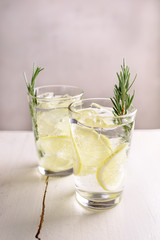 Cold fresh cocktail with lemon and rosemary on white wood table