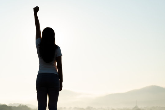 Woman With Fist In The Air During Sunset Sunrise Mountain In Background. Stand Strong. Feeling Motivated, Freedom, Strength And Courage Concept.