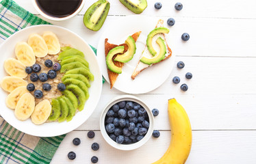Oatmeal, granola with bananas, kiwi fruits, blueberries and coffee.  Toasts with avocado. Tasty breakfast. Healthy food or diet concept.  top view. Flat lay. Copy space.