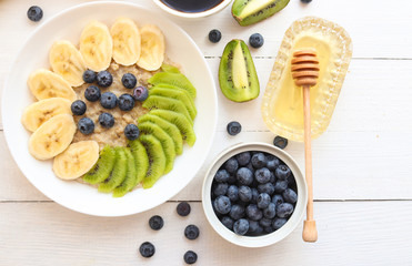 Oatmeal, granola with bananas, kiwi fruits, blueberries, honey and coffee.Tasty  vegetarian breakfast.Healthy food or diet concept.  top view. Flat lay. Copy space.