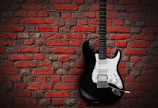 Black electric guitar on red brick wall background © SlayStorm