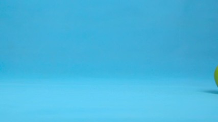 Green apple with eyes rolls slowly. Apple with rolls on a blue background. Slow motion. - Powered by Adobe