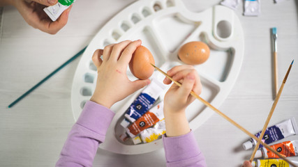 children paint easter eggs on a table with art materials