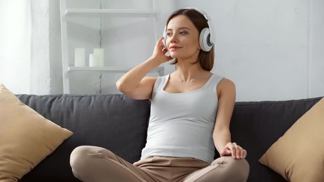 Smiling pregnant girl holding headphones near belly on couch