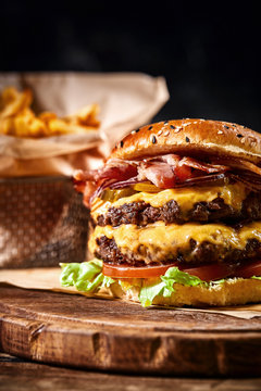 Juicy American burger, hamburger or cheeseburger with two beef patties, with sauce and basked on a black background. Concept of American fast food. Copy space