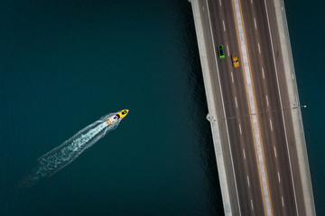 boat racing to a bridge where two cars are racing across