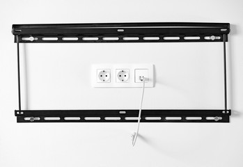 Electric outlets and network socket with coiled ethernet cable inside black metal frame for attaching the TV to wall, front view. Connection of household appliances, wiring and sources of electricity. - obrazy, fototapety, plakaty