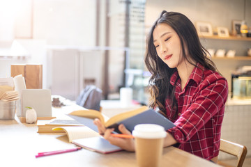 Young beautiful Asian woman reading a book while doing her homework in the modern co working space