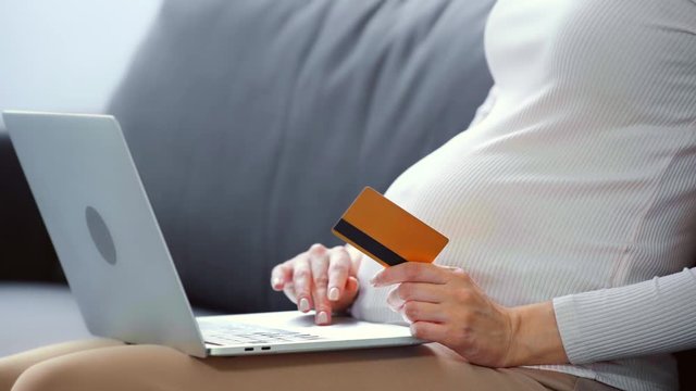 Cropped view of pregnant woman with laptop and credit card on sofa