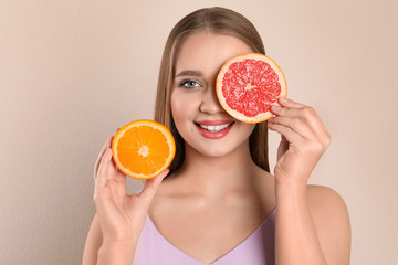 Young woman with cut orange and grapefruit on beige background. Vitamin rich food