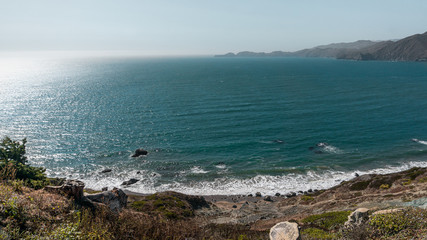 Cliff view looking over water of Pacific Ocean on clear and sunny day. Calm waves with isolated beach.