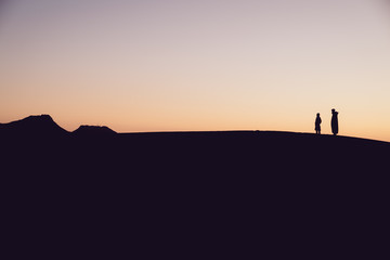 Berber desert silhouettes, father and son watching the dune landscape at sunset