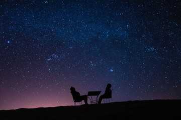 young couple sitting at a table on a desert dune while talking, relaxing and observing the stars...