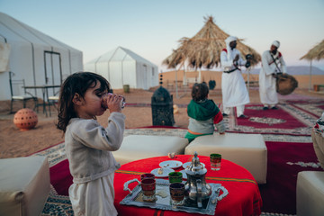 little girl drinking green tea from a typical Moroccan glass in the middle of a tent field with the...