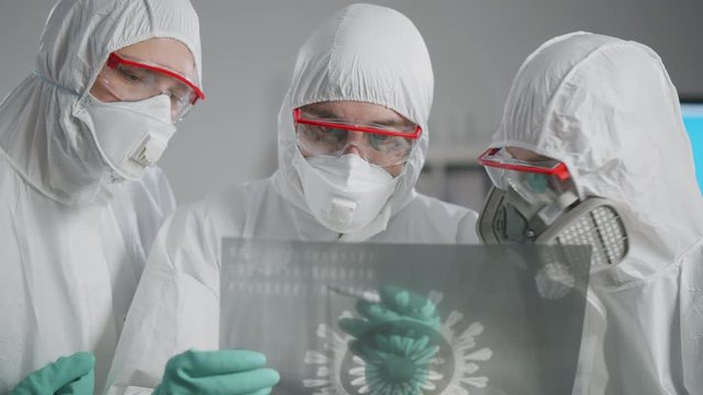 Team of scientists in protective gear looking at image of bacteria