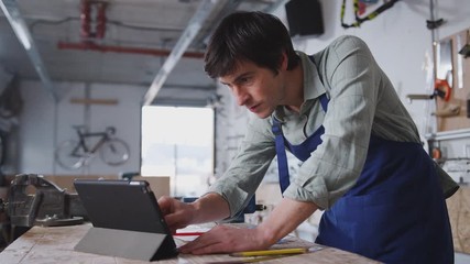 Male business owner in workshop for building bicycles using digital tablet - shot in slow motion - Powered by Adobe