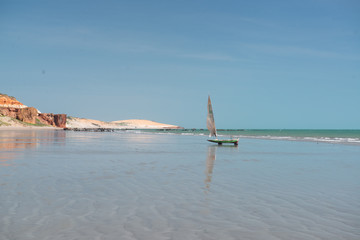 Colorful cliffs, dunes and small sailing boat early morning on the beach of Peroba, Icapui, Ceará, Brazil on April 23, 2016
