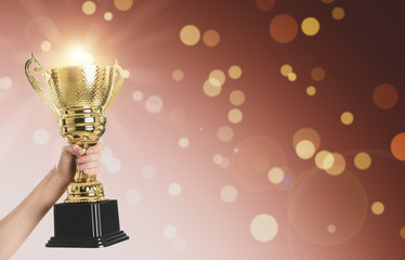 Woman holding gold trophy cup on color background, closeup. Space for text