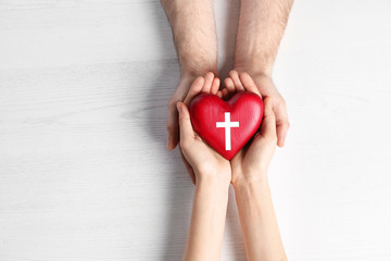 Couple holding heart with cross symbol on wooden background, top view. Christian religion