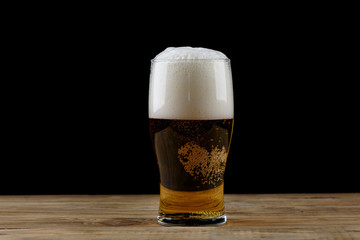 Glass of light beer with foam on a wooden table.