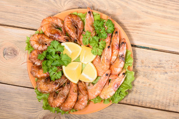 Plate with shrimps, lettuce and parsley on a wooden table.