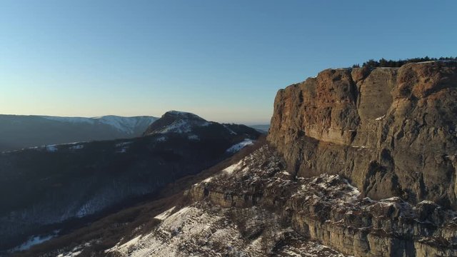 Landscape of snow covered cliffs on a suny day on blue sky background. Shot. Aerial view of sheer cliffs and green dense forest located on their slopes and down in the gorge.