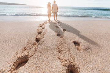 Footprints in the sand from a man and a girl at sunset