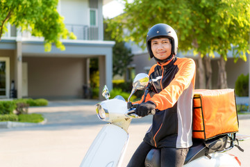 Asian man courier on scooter delivering food in town streets with a hot food delivery from take...