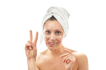 A young woman takes care of her face and smears a cream. Shows a gesture of peace and tongue. White isolated background.