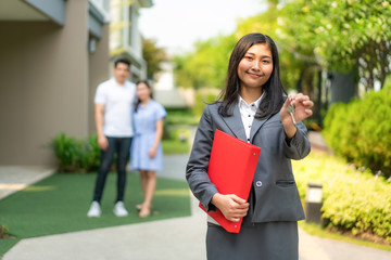 Asian real estate agent or realtor woman smiling and holding red file with showing house key with...