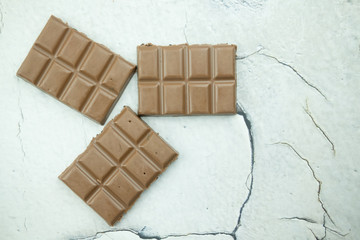 Chunks of broken dark chocolate bar on white marble background.