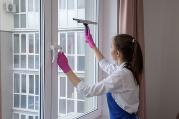 Beautiful young girl washes a window. Outside the window are multi-storey buildings.